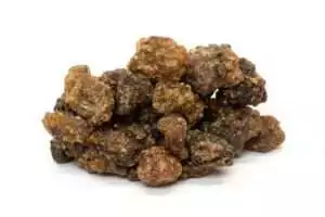 Close-up of brownish myrrh resin chunks in a loose pile — rough-textured Commiphora resin granules in natural amber-brown tones.