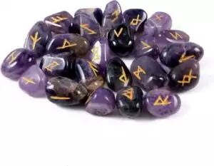Set of 25 polished amethyst Elder Futhark rune stones arranged in a circle, each carved with gold-engraved runic symbols on natural purple crystal.