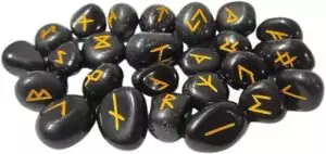 Black tourmaline rune set with 25 carved Elder Futhark stones — dark protective crystal tiles with incised Norse rune symbols for divination and warding work.