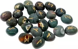 Collection of polished bloodstone rune pieces with gold Elder Futhark engravings, showing dark green stones with red iron-oxide flecks.