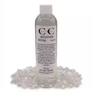 8oz Intuition Moon Water clear bottle labeled with crystal and moon imagery, sitting on a bed of small shiny crystals for psychic clarity and ritual practice.