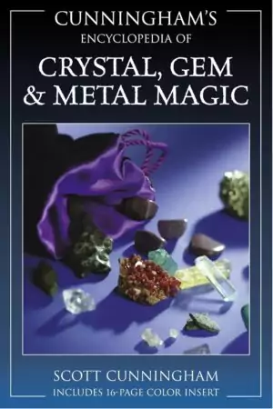 Scott Cunningham's Encyclopedia of Crystal Gem and Metal Magic book alongside various displayed crystals and gemstones on a dark surface — Llewellyn Publications.
