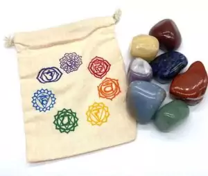 Canvas drawstring pouch with chakra symbols beside a collection of seven tumbled crystal stones one per chakra for chakra balancing meditation and energy healing