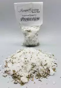 Small bag of white bath salts flecked with herbs, with a card reading Protection and a pile of the salts in front.