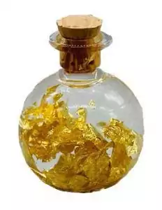 Small round glass bottle with cork stopper filled with shimmering gold metallic flakes — prosperity spell bottle for money ritual and abundance magic.