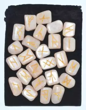 Moonstone rune set displayed on dark fabric showing golden-tinted rune symbols on polished stones — 25-piece Elder Futhark collection.