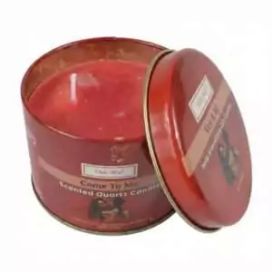 Red tin candle labeled Come To Me Scented Quartz Candle by Ohli~Way, lid slightly ajar showing crystal-chip-embedded red wax inside.