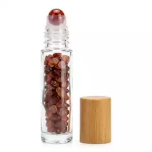 Clear glass 10ml roller bottle filled with deep red agate crystal chips, fitted with a smooth roller ball and natural bamboo cap for crystal oil blending.