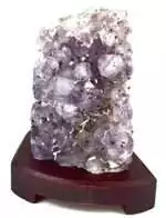 A translucent purple crystal formation displayed on a wooden stand, showcasing its natural facets and textures.
