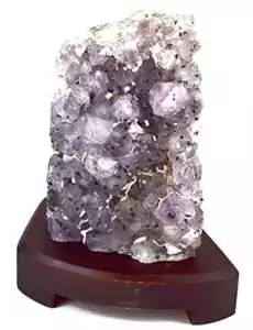 A translucent purple crystal formation displayed on a wooden stand, showcasing its natural facets and textures.