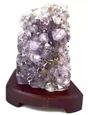 A translucent purple crystal formation displayed on a wooden stand, showcasing its natural facets and textures.