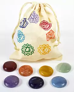 Drawstring chakra bag printed with chakra symbols displayed beside a row of seven colorful tumbled chakra stones, from red to violet.