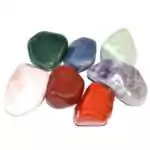 One pound of assorted mixed tumbled crystal pebbles in various colors and mineral types including greens, purples, whites, and earth tones spread across a flat surface
