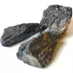 Three pounds of raw untumbled black tourmaline schorl stones in a pile showing striated black mineral surfaces and prismatic crystal structure in varied chunk sizes
