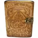 Dark faux leather journal with metal latch featuring an embossed ouija board design on the cover with planchette motif and aged interior pages