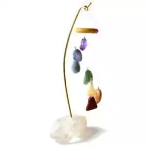Seven-rod chakra table chime with natural quartz crystal base, rainbow-colour coded rods arranged vertically, shown freestanding on plain surface