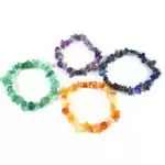 Set of seven natural stone chip bracelets in rainbow chakra colors arranged in a row on a white background, from red root to violet crown