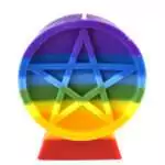 A chakra pentacle figure candle showing rainbow-layered wax in red, orange, yellow, green, blue, indigo, and violet with a pentacle symbol embossed on the front face