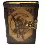 Brown embossed faux leather journal with metal latch showing a fairy sitting on a crescent moon design on the front cover, aged parchment-style pages visible