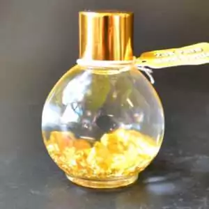 Small glass spell bottle filled with shimmering gold flake, sealed with a cork or cap, on a plain surface