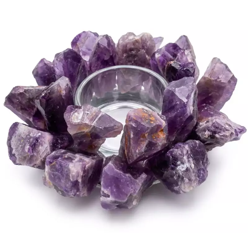 A circular arrangement of raw amethyst crystals surrounds a clear glass candle holder. The crystals are various shades of purple, creating a decorative and natural look.