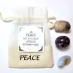 Peace Kit drawstring pouch labeled 'PEACE' with a card listing Blue Lace Agate, Lepidolite, and Botswana Agate, alongside the three polished tumbled stones displayed in front of the pouch.