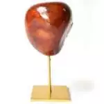Natural red agate mineral specimen on a gold-toned display stand, showing varied red and orange banding with a unique crystal form on a white background