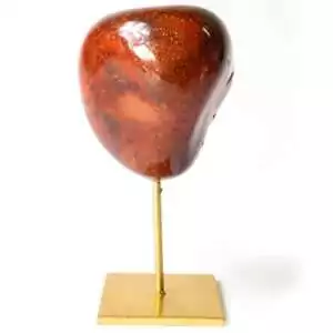 Natural red agate mineral specimen on a gold-toned display stand, showing varied red and orange banding with a unique crystal form on a white background