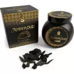 Black jar of Sonavi Amber Oud bakhoor incense chips with decorative gold lid, next to its matching box, with small oud wood pieces scattered on the surface — 40g warm amber and oud resin blend for ritual and meditation.