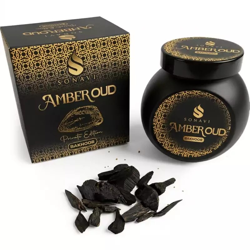 40gms-Amber-Oud-Sonavi-IBEAO40_Z Black jar of Sonavi Amber Oud bakhoor incense chips with decorative gold lid, next to its matching box, with small oud wood pieces scattered on the surface — 40g warm amber and oud resin blend for ritual and meditation.