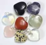 Eight heart-shaped stone pendants arranged in a circle, showing rose quartz, amethyst, red jasper, dalmatian jasper, green aventurine, black onyx, opalite, and clear quartz, each with a silver-tone jump ring.