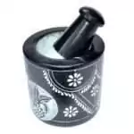 Black soapstone mortar and pestle set with a hand-carved floral vine engraving around the exterior of the bowl, pestle resting inside showing ground white powder residue.