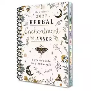 Spiral-bound Llewellyn's 2027 Herbal Enchantment Planner, a green guide to plant magic, with a cream cover of leaves, crescent moons and moths and colored month tabs down the edge.
