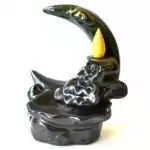 Black glazed ceramic crescent moon backflow incense burner with a sculpted eye, a yellow cone in the cone dish, and sculpted clouds above a wavy basin, on white