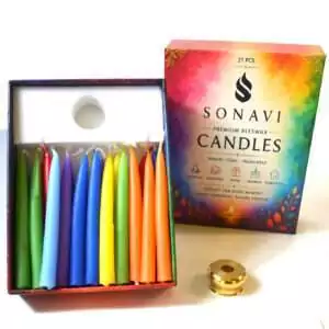 Open box of 21 assorted-color beeswax taper candles with white wicks beside the printed box lid reading Premium Beeswax Candles and a small brass candle holder